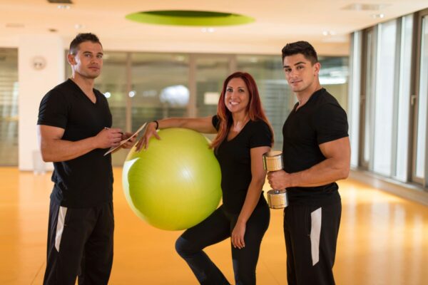 Three people are posing with a ball in the middle of a gym.